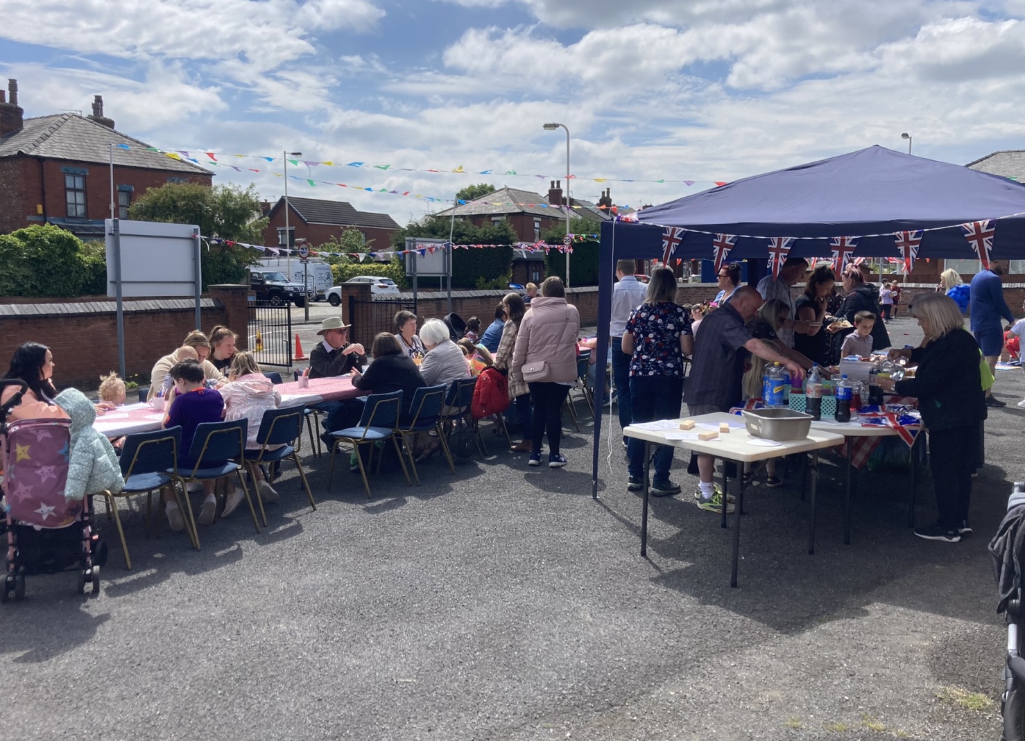 People outside enjoying food on a long table with gazebos and bunting